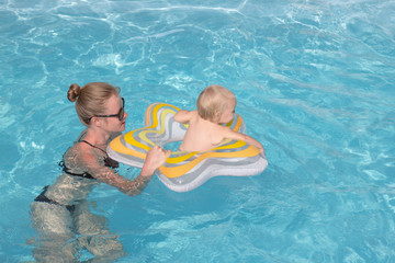 Fototapeta na wymiar young mother with one year kid swim in blue pool and having good time 