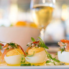 Deviled egg appetizers garnished with fresh herbs and smoked fish. Close up with blurred wine glass in the background. Square format