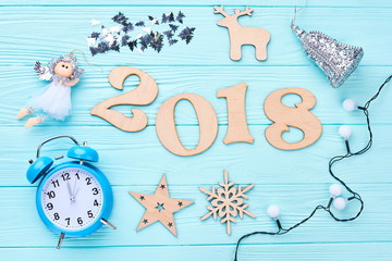 New Year 2018 decorations on wooden background. Cut out wooden digit 2018, Christmas lights, angel figurine, alarm clock, wooden silhouttes on blue wooden background, top view.