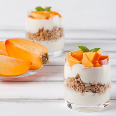 Persimmon creamy trifle in beautiful glasses, fresh ripe fruit slices on white wooden background. Healthy vegetarian food. Delicious dessert. Close up photography. Selective focus.