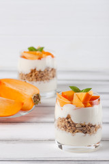 Persimmon creamy trifle in beautiful glasses, fresh ripe fruit slices on white wooden background. Healthy vegetarian food. Delicious dessert. Close up photography. Selective focus.