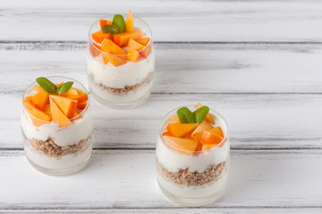 Persimmon creamy trifle in beautiful glasses, fresh ripe fruit slices on white wooden background. Healthy vegetarian food. Delicious dessert. Close up photography. Selective focus.
