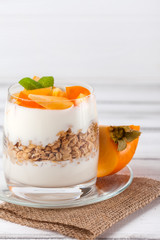 Persimmon creamy trifle in beautiful glasses, fresh ripe fruit slices on white wooden background. Healthy vegetarian food. Delicious dessert. Close up photography. Selective focus.