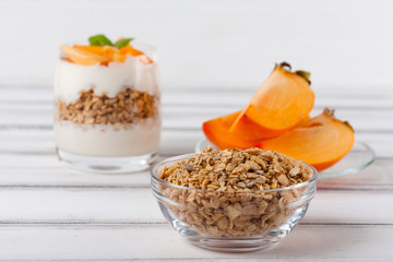 Persimmon creamy trifle in beautiful glasses, fresh ripe fruit slices on white wooden background. Healthy vegetarian food. Delicious dessert. Close up photography. Selective focus.