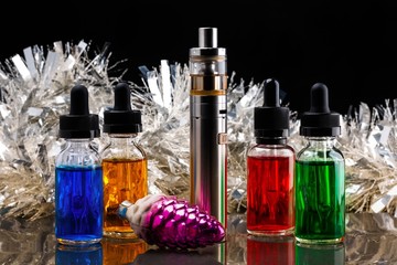 Electronic cigarette with vape liquids and christmas decorations on dark background