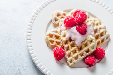 Homemade heart-shaped waffles with raspberries and  redcurrant on a white plate