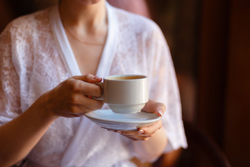 Young girl in Bathrobe with a pattern, drinking coffee on the hotel balcony, enjoying the view and the awakening. Morning girl drinking espresso. Close-up view.