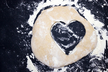 A dough heart on the table. An overhead photo of some flour, wheat dough and cookie cutter like a...