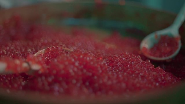 Red caviar dripping from a traditional wooden spoon. Macro food in slow motion,