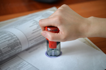 Female hand pushing rubber stamps on document at office table, closeup detail shoot.