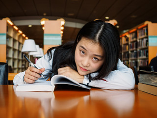 Portrait of cute Chinese girl with open book looking at camera in college library, library and education concept.