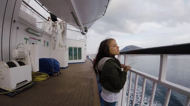 A little girl travelling on a ferry boat in the sea near a green island on a cloudy weather