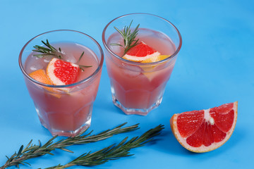 Grapefruit lemonade. Two glasses of refreshing drink, grapefruit slice and rosemary branches on blue table. Food background, recipe concept