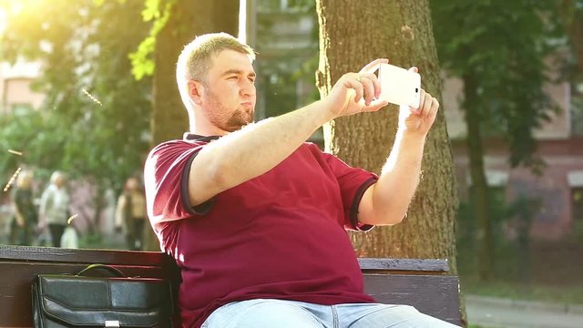 Businessman sits on the bench and records videos on smartphone. Man makes photos on his cell phone
