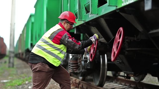 Railwayman at work. Railway worker stands near wagon of goods train on freight station and turns red wheel