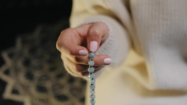 Woman, lit hand close up, counts Malas, strands of blue beads used for keeping count during mantra meditations. Time of Prayer.