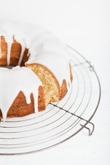 Homemade lemon bundt cake with thick lemon icing on cooling rack on white wooden table