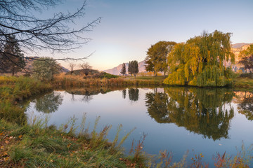 Fototapeta na wymiar Peaceful pond at sunset with reflections of surrounding trees in autumn