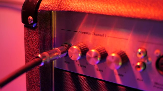 Plugging in cable into the headphone jack of amplifier. Male hand connecting and disconnecting guitar cord to amp. Red neon light. Preparing for music concert.