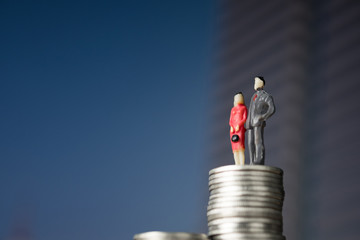 Figure miniature businessman of small people investor and office worker secretary standing on stack of coin, with modern city background for money and financial business concept.
