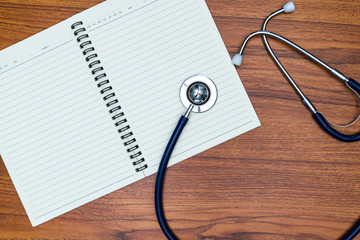 Stethoscope and notebook on wood table top view with copy space. health concept.