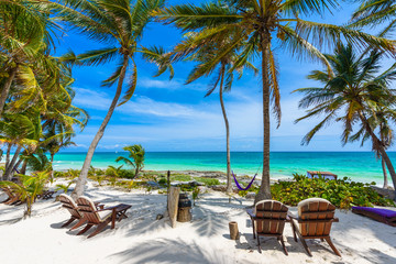 Chairs under the palm trees on paradise beach at tropical Resort. Riviera Maya - Caribbean coast at Tulum in Quintana Roo, Mexico - obrazy, fototapety, plakaty