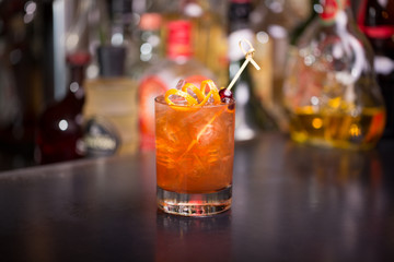 Gourmet old fashion cocktail with spiral garnish and blurry bottle background