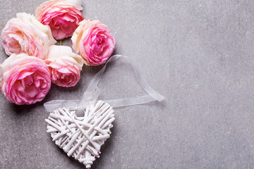 Fresh  pink roses and decorative white heart on grey slate background.