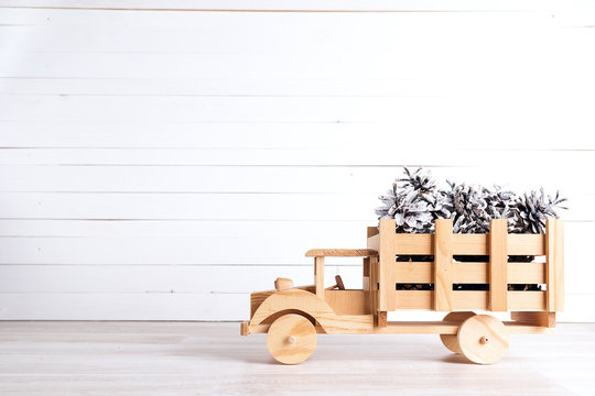 Winter holiday toy truck with snow painted pine cones on white wooden background.