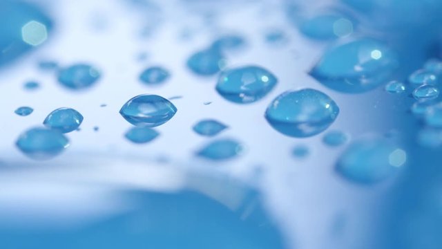 DOF, MACRO, CLOSE UP: Water droplets in high detail on water-repellent aqua blue car's roof. Transparent raindrops on blue surface. Reflecting bubbles of clear condensation on shiny blue background