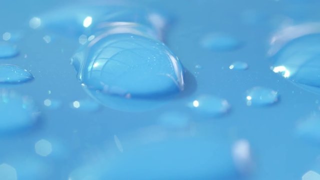 DOF, MACRO, CLOSE UP: Drops of condensation on the hood of light blue car. Highly detailed clear waterdrops on blue surface after rainfall. Reflecting transparent raindrops glistening in bright sun.