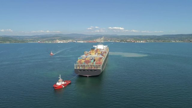 AERIAL: Fully loaded container ship coming into international ocean port. Cargo ship bringing containers filled with goods into industrial harbor. Freight ship transporting containers. Sea logistics