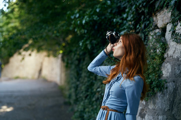 Young beautiful woman in a blue dress makes a photo on her camera in an alley on the street