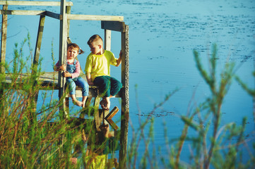 Children sit on a wooden bridge at the reservoir .Brother and sister on vacation in the countryside at sunset