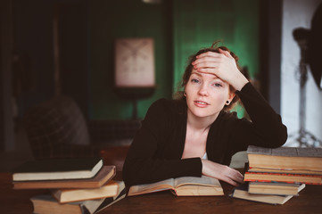 indoor portrait of thoughtful or sad redhead woman learning or reading books in university or library