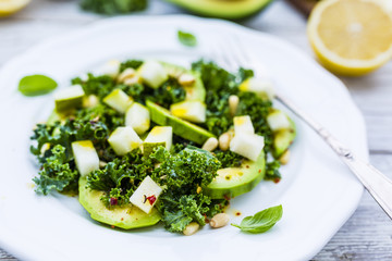 Fresh salad with kale leaves and avocado with pear on a white plate on wooden table.