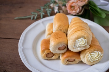 Tasty sausage rolls bread and cream horn on white plate on wooden table background