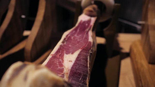 Jamon serrano.Traditional Spanish ham in the market close up.Pork leg ham on table. Gourmet Meat in restaurant interior.Whole jamon on stand.camera moving from left to right