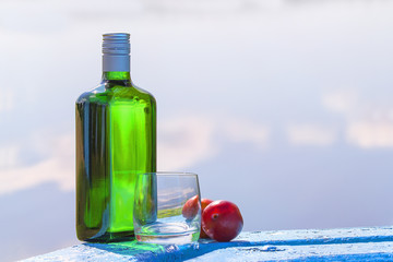 Bottle of gin with the glass and plum on the table by lake
