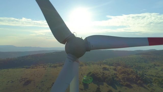 Aerial close up lone rotating windmill glistening in sunrays on spring morning