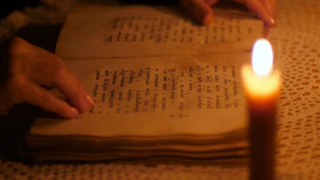 Elderly woman reading old book by candlelight
