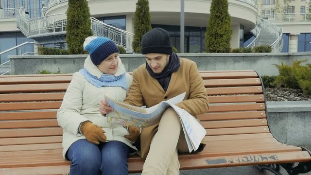 Granny with her grandson looks on the map sitting on the bench