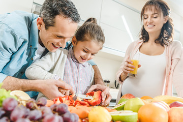 cheerful family, pregnant mother with father helping daughter slicing pepper at kitchen