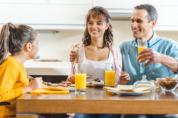 cheerful family sitting at table and holding glasses with juice at kitchen