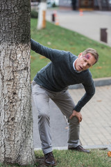 injured middle aged man with wound on head leaning on tree on the street