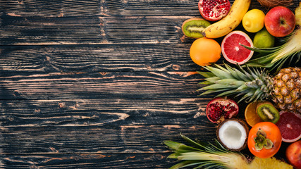 Fresh Tropical Fruits. Pineapple, coconut, kiwi, orange, pomegranate, grapefruit. On a wooden background. Top view. Free space for text.