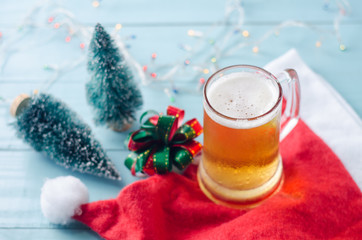 Glass of beer on christmas background with christmas tree, ribbon, santa claus hat and lights.