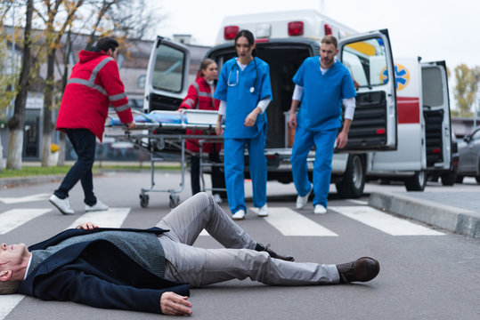 cropped image of doctors going to wounded middle aged man lying on a street