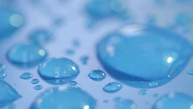 DOF, MACRO, CLOSE UP: Big and small shiny water drops on the hood of wet blue car in carwash. Transparent waterdrops on blue surface after rain. Reflecting bubbles of condensation on blue background.