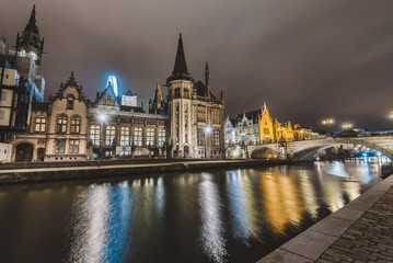 Fototapeta premium Ghent, Belgium - January, 3th, 2017. Saint Michael's bridge view with houses and Clock tower on Graslei embankment reflected in canal by evening lights. Gent night illumination. Long exposure shot.